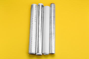 Rolls of aluminium foil, baking paper and food film on yellow background