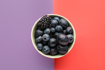 Bowl of ripe berries on color background