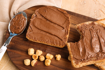 Wooden board of tasty toasts with hazelnut butter and nuts on color background, closeup