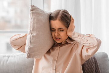 Irritated young woman with pillow suffering from loud noise at home, closeup