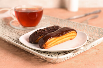 Tray with tasty chocolate eclairs and cup of tea on color table, closeup
