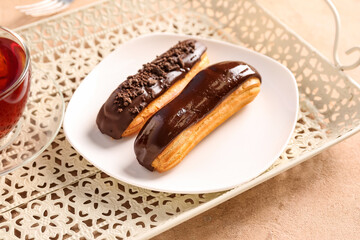 Tray with plate of tasty chocolate eclairs on color table, closeup
