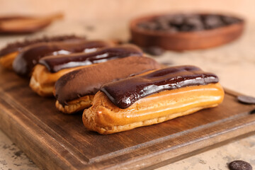 Wooden board with tasty chocolate eclairs on table, closeup