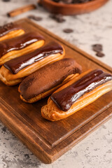 Wooden board with tasty chocolate eclairs on light background, closeup