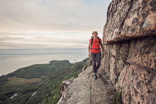 Woman hiking along cliff edge, Acadia National Park, Maine, USA - Powered by Adobe