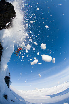 Telemark skier jumps off high cliff on sunny blue sky day in Canada backcountry near Alaska border.