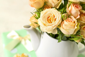 Teapot with beautiful rose flowers on light background, closeup