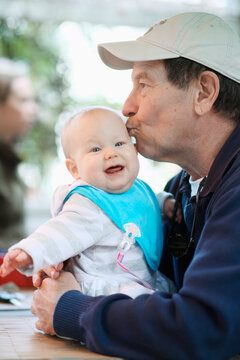 A grandfather and his baby granddaughterkiss and play and laugh outdoors.