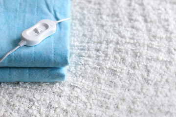 Folded electric heating pad with controller on white blanket in bedroom, closeup