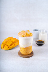 Vegan mango smoothie in plastic cup on white rustic background. Healthy drink
