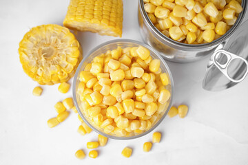 Bowl with corn kernels, tin can and cobs on white table