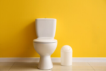 Ceramic toilet bowl and bin near yellow wall