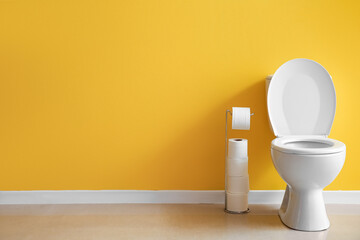 Ceramic toilet bowl and holder with paper rolls near yellow wall
