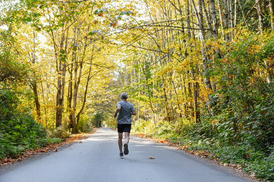 Runner jogging easily on paved road in the trees.