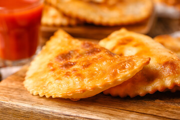 Cutting board with tasty chebureks on table, closeup