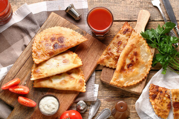 Cutting boards with tasty chebureks, parsley, tomato juice and sauce on wooden background