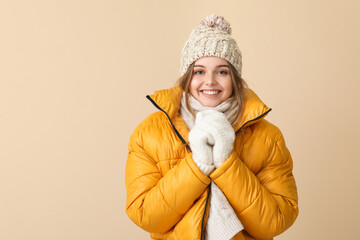 Frozen young woman in winter clothes on beige background