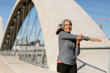 Smiling Woman Stretches Arms Before A Morning Run On A Bridge