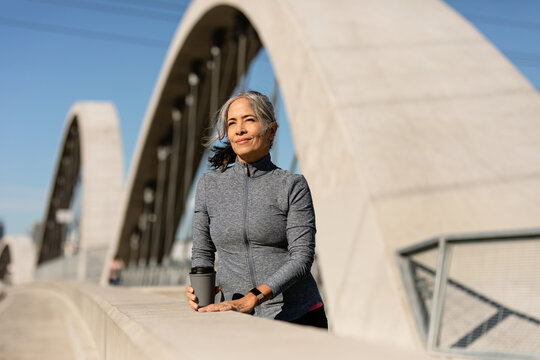 Woman Holds A Reusable Mug On A Morning Walk On A Bridge