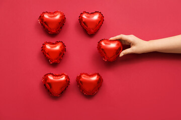 Female hand with small heart shaped balloons on color background. Valentine's Day celebration