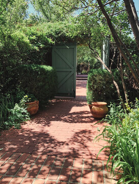 Green Wooden Gate with Lush Vegetation and Red Brick Walkway