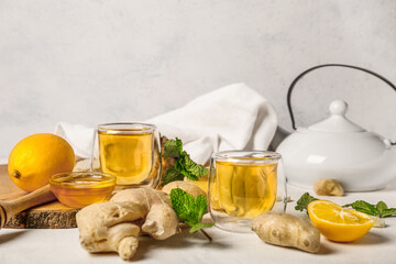 Composition with teapot, cup of tea, ginger, honey and lemon on light background