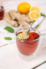 Glass cup of black tea with spoon of minced ginger on white table