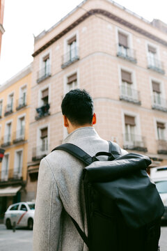 Back of young stylish man carrying a backpack in sunlight in the city
