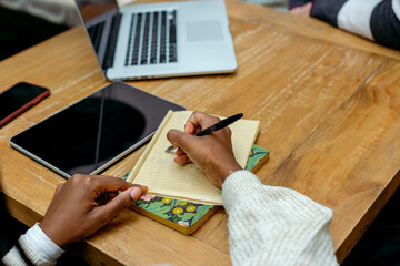 Anonymous hands writing ideas on notebook in business meeting at cafe