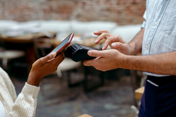 Anonymous hands paying the bill of cafeteria with mobile phone