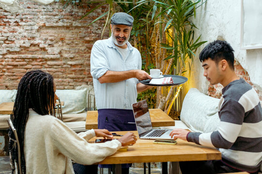 Cafe server bringing coffee cups to young customers on a table