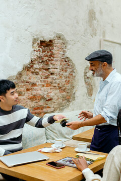 People in cafe interacting with waiter while paying with mobile phone