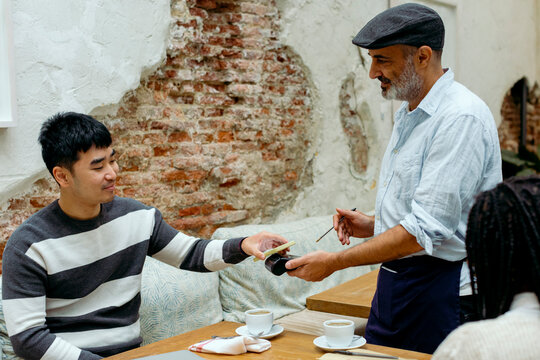 Man in cafe interacting with waiter while paying with mobile phone