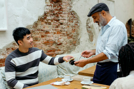Man in cafe interacting with waiter while paying with mobile phone