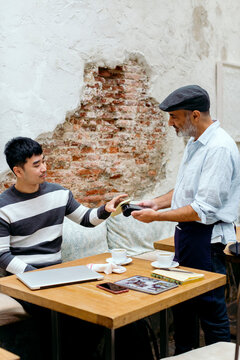 Man in cafe interacting with waiter while paying with mobile phone