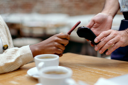 Anonymous hands paying the bill of cafeteria with mobile phone