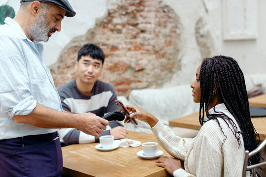 Woman in cafe interacting with waiter while paying with mobile phone