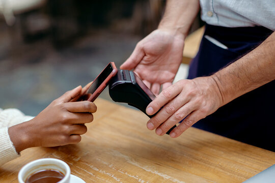Anonymous hands paying the bill of cafeteria with mobile phone