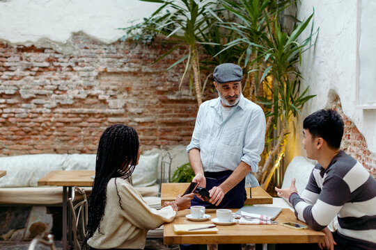 People in cafe interacting with waiter while paying with mobile phone