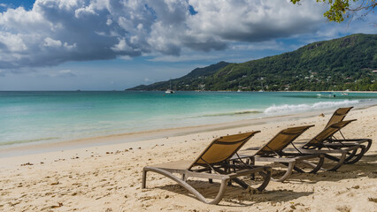 Deck chairs are in a row on a tropical beach. The waves of the turquoise ocean are foaming on the...