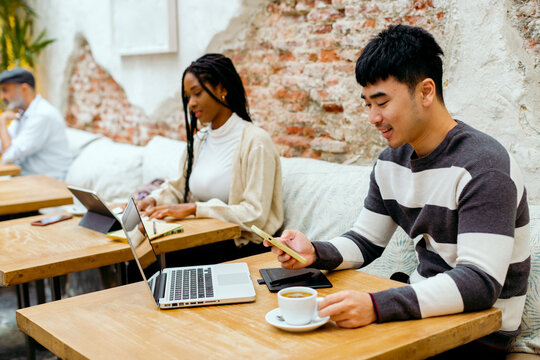 Young man using his cell phone while having coffee in modern cafe