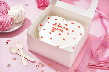 Opened box with tasty bento cake, zephyr and confetti on pink table. Valentine's Day celebration