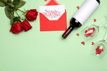 Fototapeta na wymiar Bottle of wine, greeting card in envelope, rose flowers and glasses on green background. Valentine's Day celebration