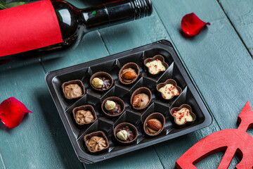 Box with candies, bottle of wine and rose petals on grey wooden background, closeup. Valentine's Day celebration