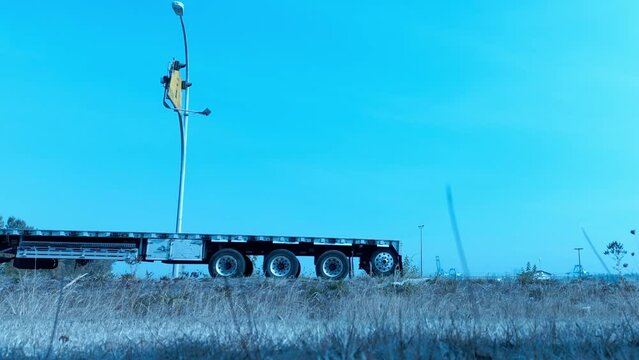 Loop video transport truck red with empty flatbed trailer lowboy six wheeler followed by white sports car and another gray vehicle 4 door sedan on a clear blue day. Easy repeat continuous playback