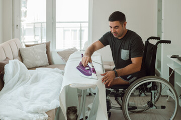 An adult man on a wheelchair irons things with an electric iron.