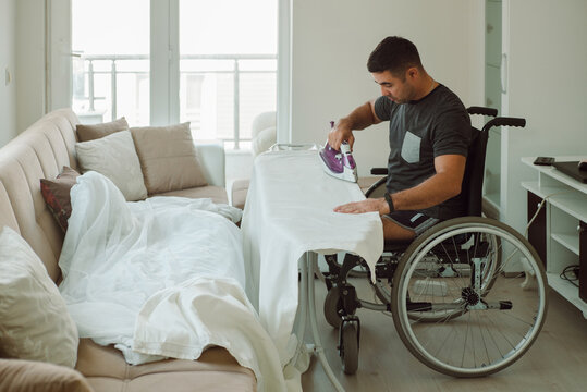 An adult man on a wheelchair irons things with an electric iron.