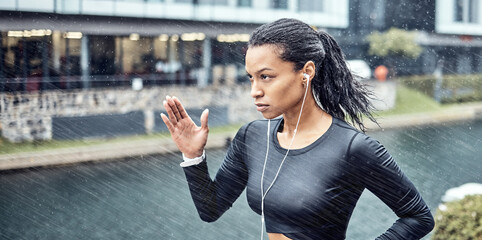 Black woman, fitness and running with earphones in the rain for sports motivation or determination...