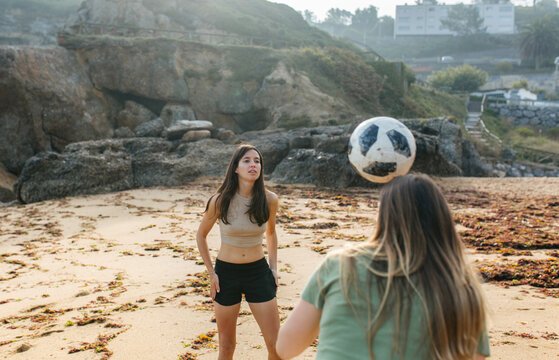 Two young women playing with ball on sandy beach