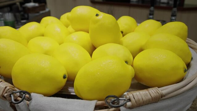 Bright yellow lemons in a bowl on display, glistening with condensation.